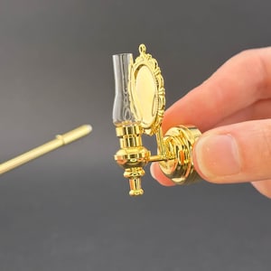 Può includere: Applique da parete in miniatura dorata con un paralume in vetro trasparente e uno specchio rotondo piccolo. L'applique è in stile tradizionale.
