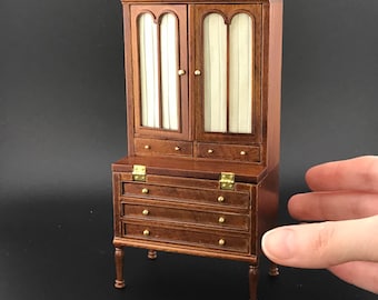 May include: A wooden cabinet with a glass-front top section and three drawers below. The cabinet has a dark brown finish and ornate carvings on the top.