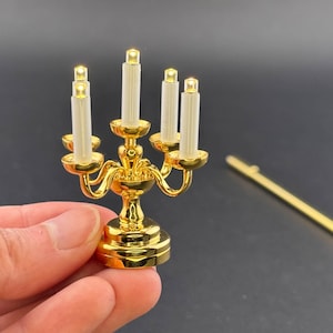 以下が含まれることがあります： 5本の白いLEDキャンドルが付いた金色の燭台。燭台は装飾的なベースと曲線的なデザインをしています。