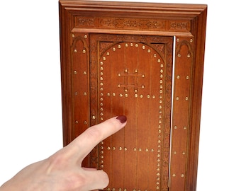 May include: A miniature wooden door with a detailed design. The door is a warm brown color, adorned with small brass studs and decorative carvings. The door is part of a miniature set, perfect for dollhouses or craft projects.