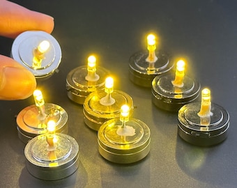 May include: A set of nine small, round, battery-operated LED tea lights. The lights are in silver and gold metal holders and emit a warm yellow glow.