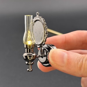 May include: A miniature silver-colored wall sconce with a round mirror and a glass lampshade. The lampshade has a small light bulb inside.