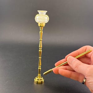 Könnte beinhalten: Goldene Stehlampe mit einem klaren Glasschirm. Die Lampe wird mit einem separaten Stangenstück montiert.