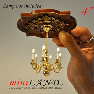 May include: A miniature gold chandelier with 6 candle-style lights hangs from a decorative wooden ceiling medallion. The medallion is 10 cm in diameter and has a floral design. The text "Lamp not included" is visible in the image.