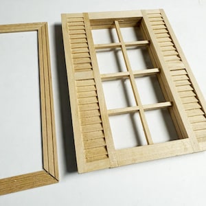 Op de afbeelding: Een miniatuur houten raamkozijn en luikenset. Het raam heeft een raster van kleine ruiten en lamellen. Het hout heeft een natuurlijke, lichtbruine kleur en is ontworpen voor een poppenhuis of knutselproject.