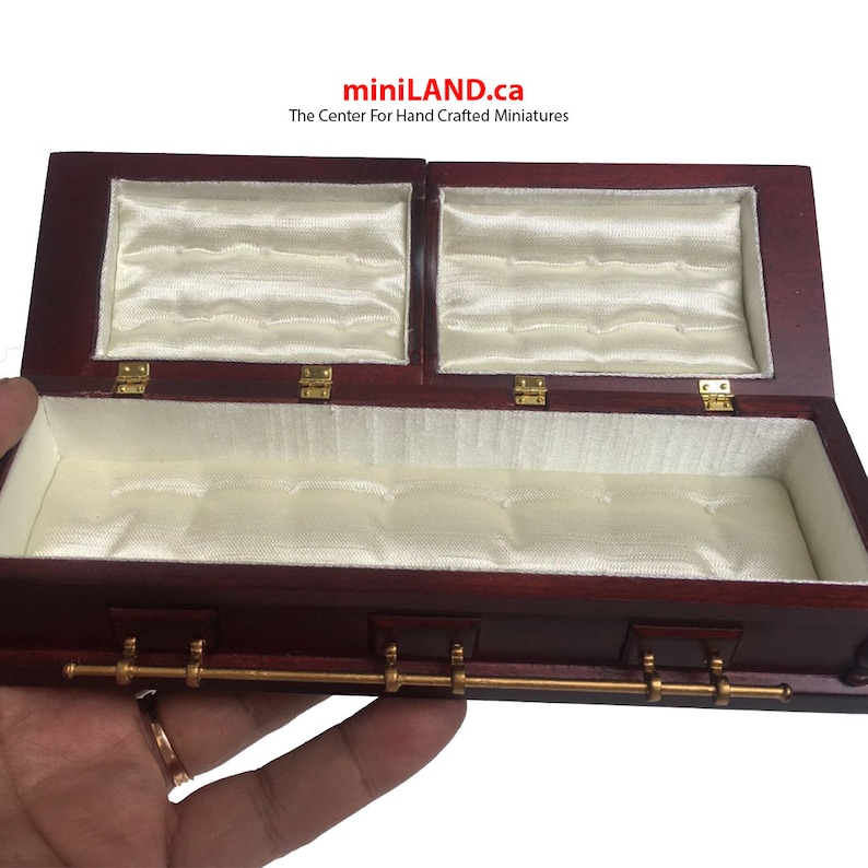 May include: A miniature wooden coffin with a satin lining and gold-coloured hardware. The coffin is open and the lid is propped up.