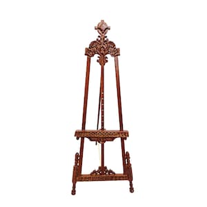 Può includere: Un cavalletto da artista in legno marrone con intagli ornati. Il cavalletto ha una parte superiore decorativa, un supporto per tela e gambe regolabili. Il legno ha una tonalità ricca e calda e il design è dettagliato ed elegante.