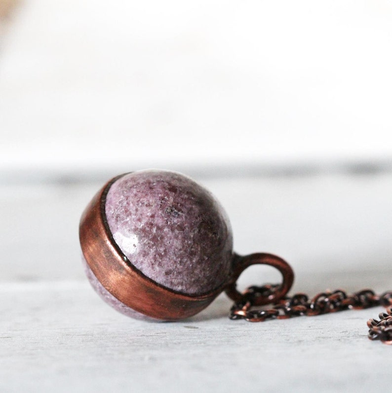May include: A copper pendant necklace with a round, purple and white stone. The stone has a speckled pattern.