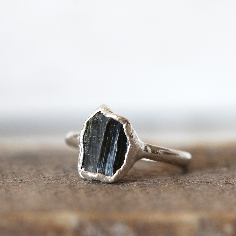 Puede incluir: Un anillo de plata con una piedra preciosa de turmalina negra. El anillo est&aacute; engastado con una piedra en bruto sin cortar.