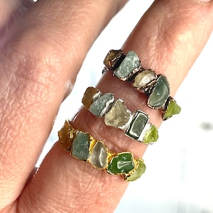 May include: Three gold rings with green and clear stones. Each ring has a different style of setting.