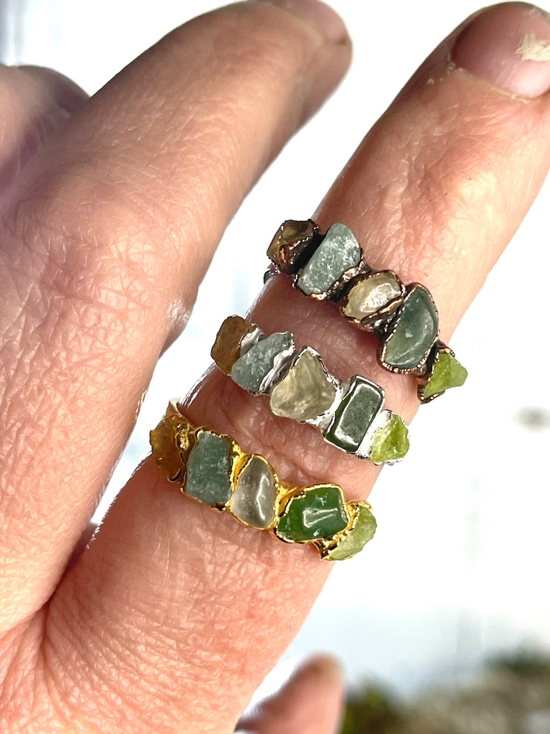 May include: Three gold rings with green and clear stones. Each ring has a different style of setting.