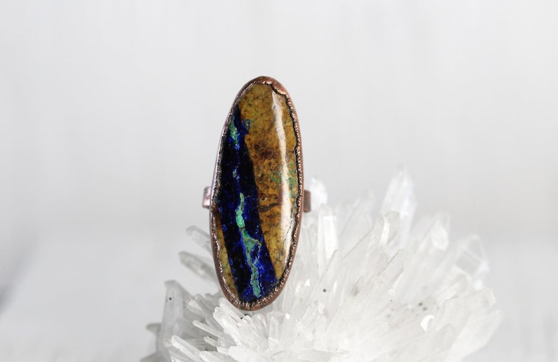 May include: Oval-shaped ring with a copper setting and a blue and brown stone. The stone has a unique pattern of blue and brown swirls.