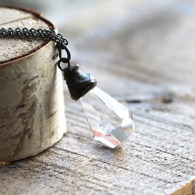 May include: A silver chain necklace with a clear crystal pendant. The pendant is faceted and has a silver cap at the top.