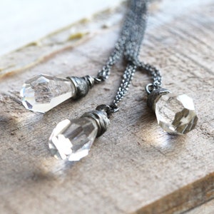 May include: A silver chain necklace with three clear crystal pendants. Each pendant is wrapped in silver wire.
