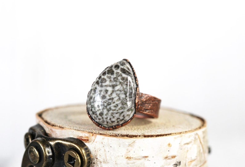 May include: A teardrop-shaped ring with a white and gray fossilized stone set in a copper band.