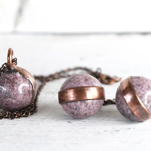 May include: A copper chain necklace with three pink and white marble sphere pendants. Each sphere has a copper band around the middle.