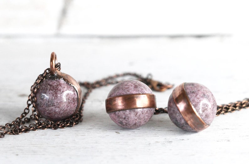 May include: A copper chain necklace with three pink and white marble sphere pendants. Each sphere has a copper band around the middle.