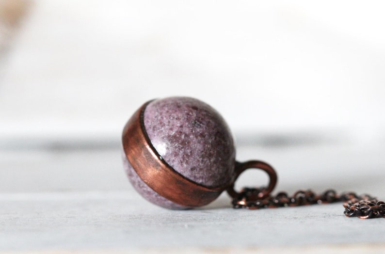 May include: A copper and purple stone pendant necklace. The pendant is a sphere with a copper band around the middle. The necklace is made of a copper chain.