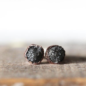 May include: A pair of black diamond earrings with copper settings. The diamonds are rough and have a natural, raw look.