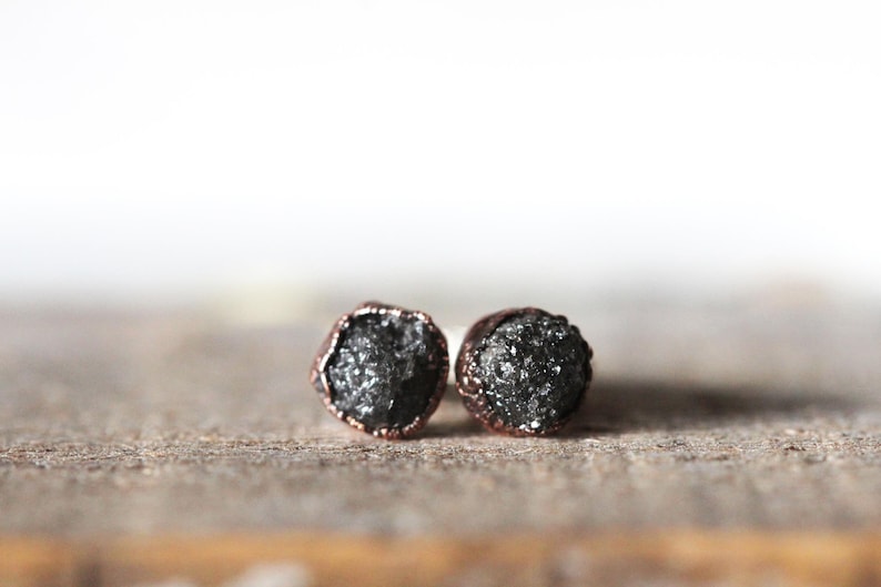 May include: A pair of black diamond earrings with copper settings. The diamonds are rough and have a natural, raw look.