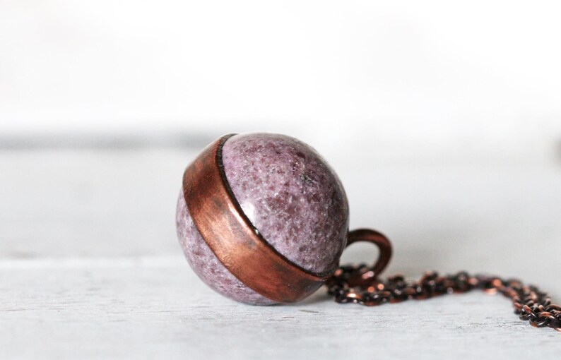 May include: A copper and purple stone pendant necklace. The pendant is a sphere with a copper band around the middle. The necklace is made of a copper chain.