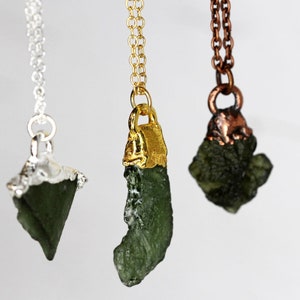 May include: Three necklaces with green gemstone pendants. The pendants are different shapes and sizes. The necklaces are silver, gold, and copper.