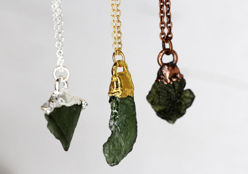 May include: Three necklaces with green gemstone pendants. The pendants are different shapes and sizes. The necklaces are silver, gold, and copper.