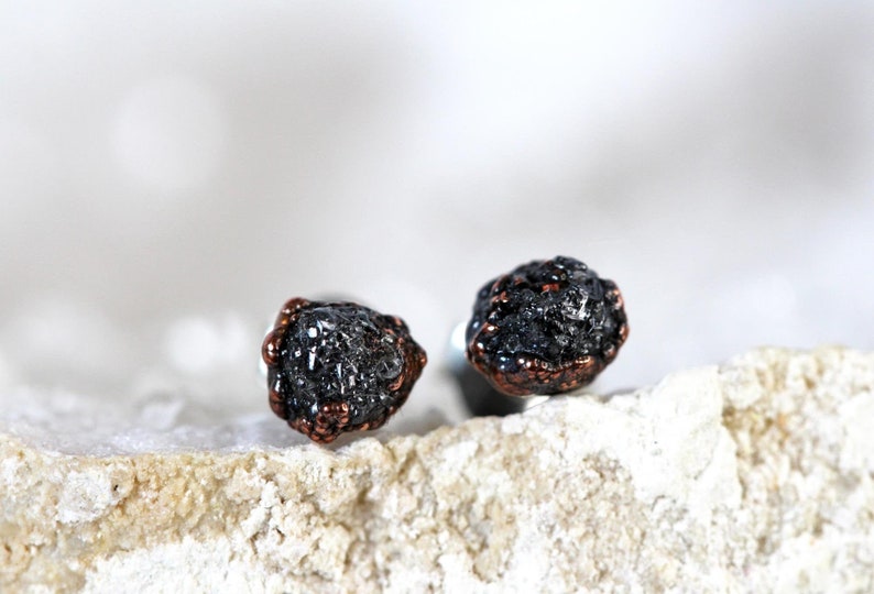 May include: A pair of black diamond earrings with copper accents. The earrings are set in silver and have a rough, natural look.
