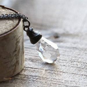 May include: A silver chain necklace with a clear crystal pendant. The pendant is faceted and has a silver cap at the top.