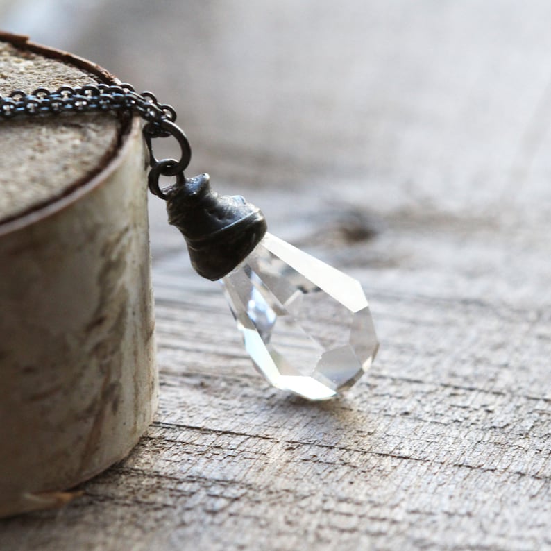 May include: A silver chain necklace with a clear crystal pendant. The pendant is faceted and has a silver cap at the top.