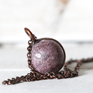 May include: A copper chain necklace with a round pendant made of pink and white speckled stone.