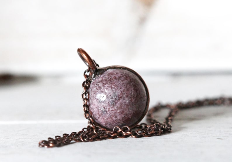 May include: A copper chain necklace with a round pendant made of pink and white speckled stone.