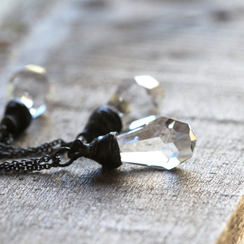 May include: A silver chain necklace with three clear crystal pendants. Each pendant is a faceted, geometric shape and is attached to a silver cap.