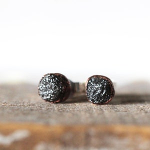 May include: A pair of black diamond stud earrings with copper wire accents. The earrings are set in silver.