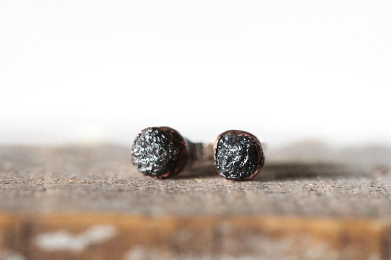 May include: A pair of black diamond stud earrings with copper wire accents. The earrings are set in silver.