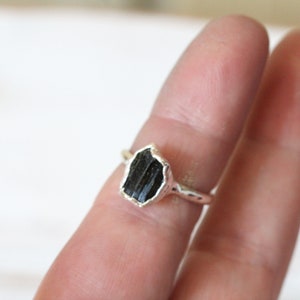 Puede incluir: Un anillo de plata con una piedra preciosa de turmalina negra. El anillo est&aacute; en un dedo.