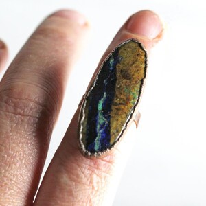May include: A copper ring with a large oval-shaped stone set in the center. The stone is a mix of blue, green, and brown colors.