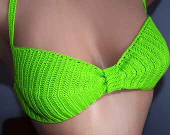 Könnte beinhalten: Ein neongrünes Häkel-Bikini-Oberteil mit texturiertem Zickzack-Muster, dünnen Trägern und einem mittigen Knoten-Detail an der Brust. Das Kleidungsstück ist aus leuchtend limettengrünem Garn mit einem gleichmäßigen, wiederkehrenden Strickmuster gefertigt.