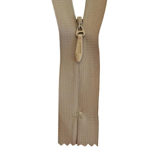 May include: A beige nylon coil zipper featuring a matching beige pull tab and slider. The zipper tape is made of a woven fabric, and the teeth are integrated into the tape, creating a smooth, continuous appearance when closed.