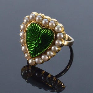 May include: A gold ring with a heart-shaped green enamel design surrounded by a border of white pearls.