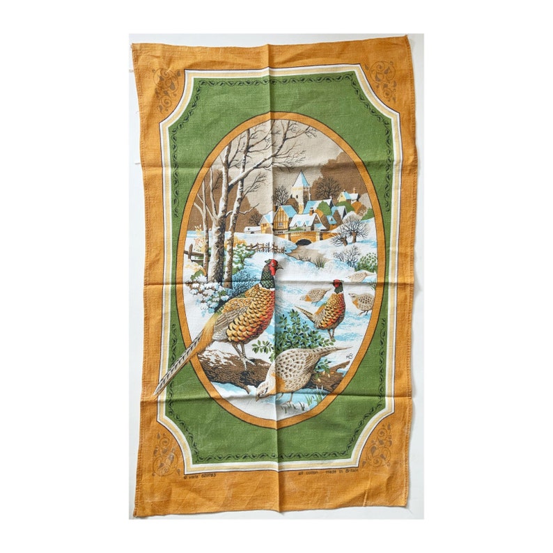 May include: A vintage kitchen towel featuring a winter scene with pheasants. The central oval design shows a snowy landscape with a village and a bridge. The towel has a green and gold border, with the pheasants in the foreground.