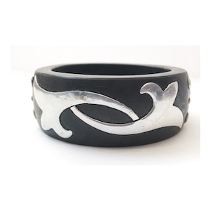 May include: Black wooden bangle with a silver floral design. The bangle is decorated with small silver studs.