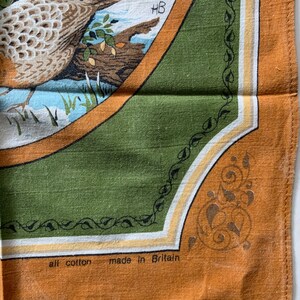 May include: A vintage cotton tea towel with a detailed illustration of a bird in a natural setting. The design is framed by a green border with decorative elements and the text "all cotton made in Britain".