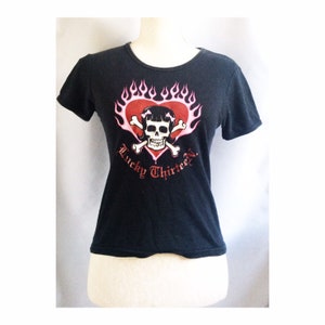 May include: Black t-shirt with a pink and red graphic of a skull with pigtails inside a heart with flames. The text "Lucky Thirteen" is below the graphic.
