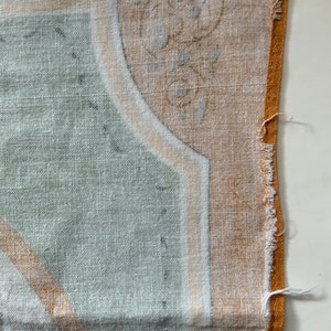 May include: Close-up of a section of fabric with a detailed pattern. The design features a combination of light green, white, and tan colors. The fabric has a textured appearance, with a frayed edge on the right side.