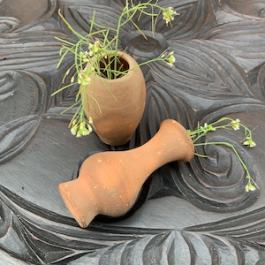 May include: Two small terracotta vases with white flowers, sitting on a dark wood surface with a carved design.