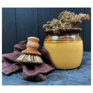 May include: A wooden brush with natural bristles sits on a brown cloth next to a yellow ceramic pot with dried flowers.