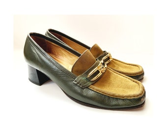 May include: Green leather heeled loafers with a brown suede toe and gold chain detail.