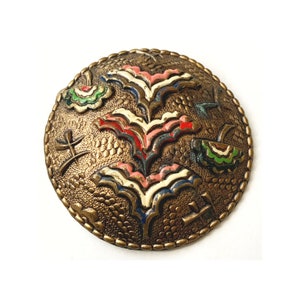 May include: A round, gold-toned brooch with a raised, textured design. The design features stylised flowers in shades of pink, red, green, and blue.