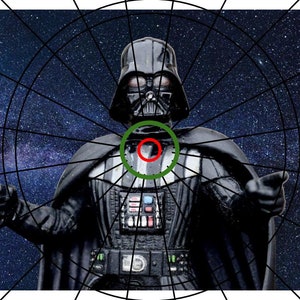 May include: Darth Vader action figure with a black and silver suit, standing against a dark blue background with white stars. The figure has a red and green target on its chest.